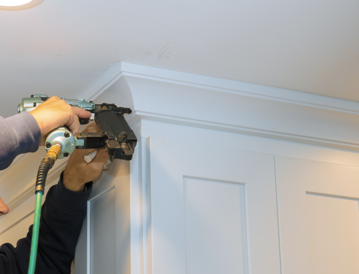 cabinet crown moldings Person using a nail gun to install crown molding on a white cabinet.